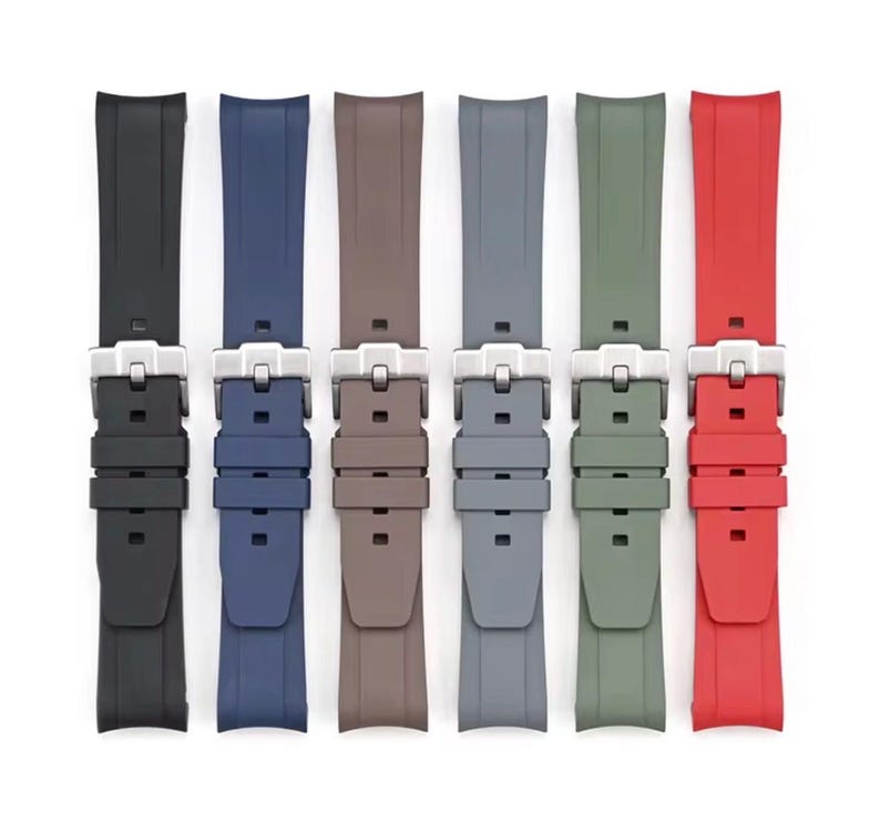 May include: Six watch straps in a range of colours: black, navy, brown, grey, olive green, and red. Each strap has a silver-coloured buckle. The straps are displayed against a white background.
