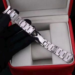 Pu&ograve; includere: Un cinturino per orologio in metallo color argento con finitura lucida e un meccanismo di chiusura deployante sicuro. Il cinturino a maglie &egrave; progettato con un terminale curvo per il fissaggio alla cassa dell'orologio, con una struttura classica.
