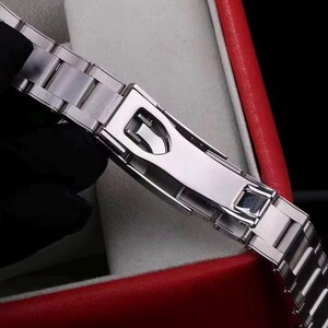Pu&ograve; includere: Un cinturino per orologio in metallo color argento con finitura lucida e un meccanismo di chiusura deployante sicuro. Le maglie sono rettangolari e collegate in un design standard a tre pezzi, con una superficie liscia e riflettente.