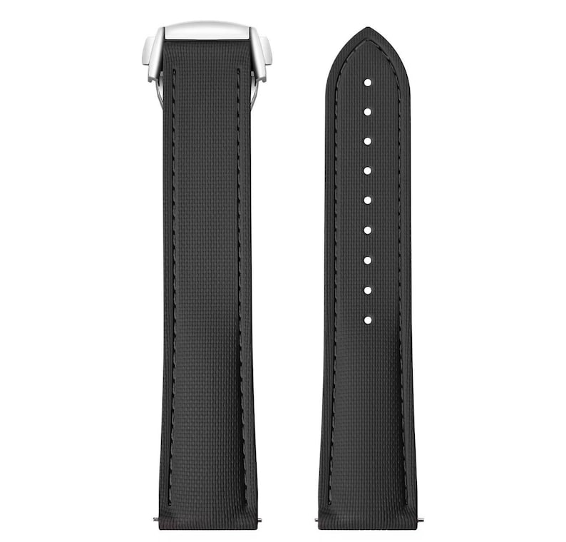 May include: A black watch strap with a textured surface and white metal clasp. The strap has a series of holes for adjustment and is designed to attach to a watch face. The strap is shown against a white background.