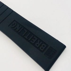 May include: A black rubber watch strap featuring the embossed text BREITLING and the numbers 24-20 235S. The strap has a smooth, matte finish with horizontal ridges near the top edge, designed for a secure fit on a timepiece.