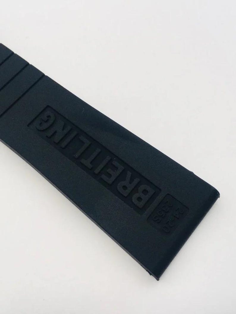 May include: A black rubber watch strap featuring the embossed text BREITLING and the numbers 24-20 235S. The strap has a smooth, matte finish with horizontal ridges near the top edge, designed for a secure fit on a timepiece.