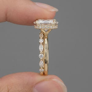 May include: A gold ring featuring a large rectangular center stone set in a halo of small round diamonds. The band is adorned with alternating marquise and round diamonds, creating a detailed profile view of the setting and the intricate metalwork.