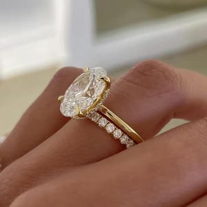 May include: A gold engagement ring featuring a large oval-cut center stone held by four prongs, paired with a matching gold wedding band. Both rings are adorned with small round-cut diamonds along the band, creating a cohesive set.
