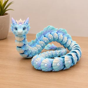 May include: A serpentine dragon figurine featuring a gradient of light blue and lavender colors. The body is composed of articulated, shell-like segments, each accented with a small, round, white pearl-like bead. The head has two horns.