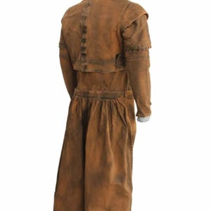 Op de afbeelding: Een bruin kostuum in vintage-stijl met een lange jas en bijpassende rok. De outfit heeft een getailleerd lijfje, lange mouwen en een geplooide rok. De stof lijkt een versleten, getextureerd materiaal te zijn, waardoor het een versleten uiterlijk heeft.