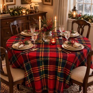 May include: A round dining table covered with a red, green, and yellow plaid tablecloth, set with white plates, napkins with berry sprigs, clear glasses, silverware, and a central glass vase containing a festive holiday floral arrangement.