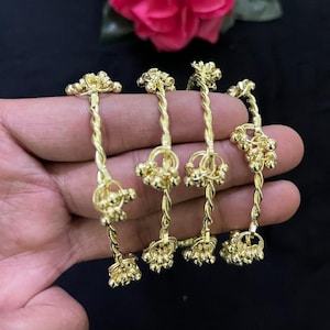 Könnte beinhalten: Vier goldfarbene Armreifen mit einem gedrehten Metalldesign. Jeder Armreif ist mit kleinen, hängenden goldfarbenen kugelförmigen Anhängern verziert, die entlang des gedrehten Bandes verteilt sind und ein zartes, reflektierendes Aussehen erzeugen.