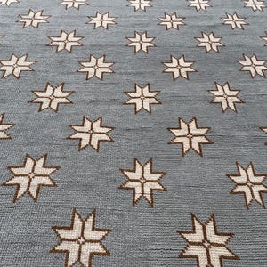 May include: A rectangular area rug featuring a light blue background with a repeating pattern of white eight-pointed star motifs. The rug has a textured, woven surface with a consistent grid-like arrangement of the star shapes across the entire piece.