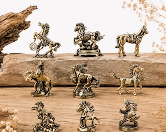 Puede incluir: Una colección de nueve figuras de caballos de color bronce en varias poses. Algunos caballos se alzan, otros están de pie y algunos están adornados con sillas de montar o elementos decorativos. Las figuras se exhiben sobre una superficie de madera.