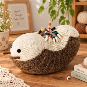 May include: A knitted plush toy shaped like a pill bug with a cream-colored head and a dark brown segmented body. It features two small antennae, black button eyes, and a row of small, multi-colored legs along the top of its back.
