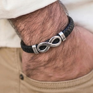 Pode incluir: Uma pulseira de couro trançado preto com uma peça central em forma de símbolo do infinito prateado. Os componentes metálicos estão gravados com os nomes Jackson e Lucilla, e o centro do laço infinito tem o texto Forever Love.