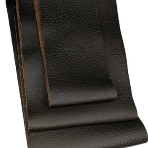 Könnte beinhalten: Nahaufnahme von dunkelbraunen Lederstreifen mit strukturierter Oberfläche. Das Leder hat eine natürliche Maserung und eine satte, tiefe Farbe. Die Kanten des Leders sind sichtbar und zeigen die Dicke und Qualität des Materials.