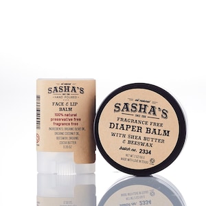 May include: Two brown and black labeled containers of natural skin care products. The smaller container is a stick balm labeled "Sasha's Face & Lip Balm" with the text "100% natural preservative free fragrance free" and ingredients listed. The larger container is a round jar labeled "Sasha's Fragrance Free Diaper Balm with Shea Butter & Beeswax" with the text "batch no. 2334" and "Net Wt 2 oz/56 g".
