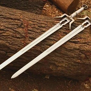 May include: Two long metal swords with silver-toned blades and pointed tips. Each sword features a distinct crossguard with a cutout design near the hilt. One sword has a white handle, while the other has a black handle, both ending in a circular pommel.
