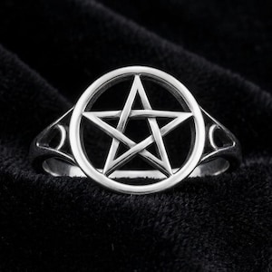 Puede incluir: Anillo plateado con un diseño de pentagrama dentro de un marco circular. El anillo tiene un diseño calado detallado en la banda, sobre un fondo oscuro. El pentagrama es una estrella de cinco puntas, un símbolo a menudo asociado con la Wicca y el paganismo.