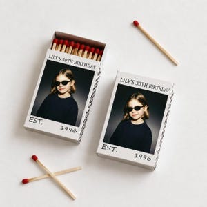 May include: Two rectangular matchboxes featuring a custom photo of a person wearing sunglasses. The text reads LILY'S 30TH BIRTHDAY and EST. 1996. One box is open, revealing red-tipped wooden matches, while three loose matches lie nearby.