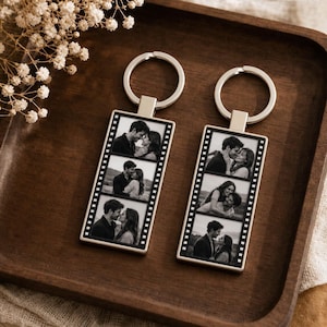 Puede incluir: Dos llaveros rectangulares de metal con un diseño de tira de película en blanco y negro. Cada llavero muestra tres fotografías distintas en blanco y negro de una pareja en varias poses, unidas a una anilla metálica de color plateado.