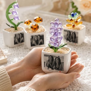 May include: A square white ceramic planter containing a purple glass flower sculpture and light-colored gravel. The front of the planter features a black and white photograph of two people and the text "Whatever Forever" with a small red heart.