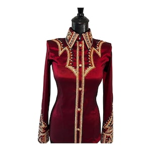 May include: A long-sleeved, deep burgundy button-down shirt featuring a structured collar and intricate embellishments. The front yoke, collar, and cuffs are adorned with gold, black, and clear crystals arranged in geometric patterns.