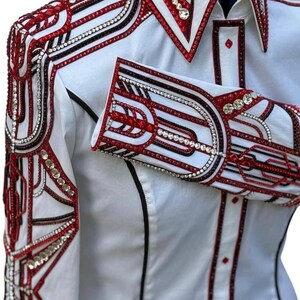May include: White button-up shirt with intricate red, black, and silver embellishments. The design features geometric patterns and sparkling accents on the collar, cuffs, and shoulders. A black trim outlines the shirt's edges.