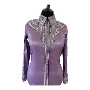May include: A long-sleeved lavender shirt featuring a structured collar and button-down front. The garment is heavily embellished with silver-toned studs, clear crystals, and intricate beadwork along the collar, shoulders, and front placket.