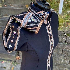 May include: A black equestrian show jacket with elaborate embellishments. The jacket features silver, rose gold, and clear crystal accents. The design includes geometric patterns and sparkling details, creating a glamorous look.