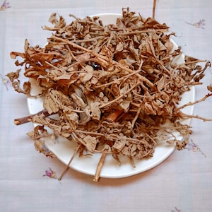 May include: A pile of dried brown plant stems and leaves resting on a round white plate. The botanical material consists of brittle, withered foliage and thin woody stalks, creating a textured, layered appearance within the circular dish.