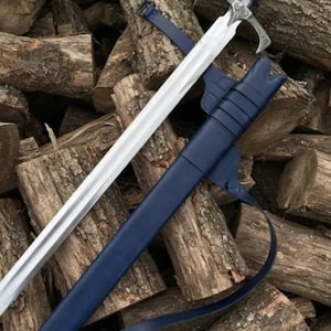 Op de afbeelding: Een langzwaard met een gepolijst stalen lemmet, een donkerblauw handvat en een versierde zilverkleurige pareerstang. Het zwaard wordt vergezeld door een bijpassende donkerblauwe schede met zilverkleurige metalen beslag aan de punt en een dunne leren riem.
