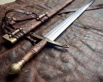 Peut inclure: Une épée en acier avec un manche en bois, un pommeau en laiton et une garde ornée de motifs gravés. L'épée est accompagnée d'un fourreau en cuir marron assorti avec des motifs gaufrés complexes, des accents en laiton et des lanières en cuir.