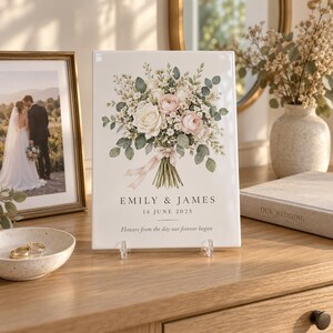 May include: A rectangular white ceramic plaque featuring a floral bouquet illustration with pink and white roses, green leaves, and a ribbon. The text reads EMILY & JAMES, 14 JUNE 2025, and Flowers from the day our forever began in black font.