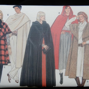 May include: A sewing pattern envelope featuring illustrations of five different cape and cloak designs labeled A, C, D, and E. The designs include a red plaid cape, a cream wrap, a long black hooded cloak, a red hooded cape, and a brown textured cape.