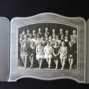 May include: Black and white photo of a group of people, mostly women, in a formal setting. The photo is framed in a silver frame with a scalloped edge. The photo is dated "May 1924".