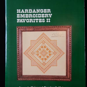 May include: A green book titled "Hardanger Embroidery Favorites II" with a framed embroidery design on the cover. The design features a geometric pattern in shades of orange and cream. The authors' names are listed at the bottom.