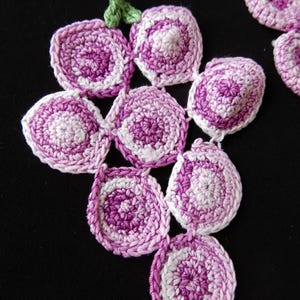 May include: A crocheted grape cluster with a green stem. The grapes are made with a pink and white yarn, creating a gradient effect.