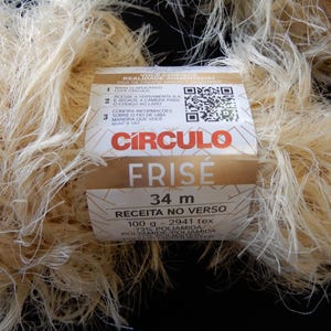 May include: Close-up of a skein of light beige Circolo Frise yarn. The label indicates 34 meters of yarn, 100 grams, and 73% Polyamide. The yarn has a textured, frizzy appearance, ideal for various crafting projects.