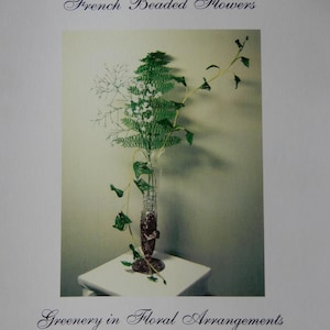 May include: A book cover titled French Beaded Flowers: Greenery in Floral Arrangements by Donna DeAngelis Dickt. The cover features a photograph of a clear glass vase containing green beaded fern and ivy stems with white accents.
