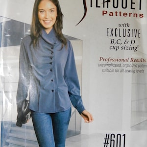 May include: A woman wearing a blue asymmetrical blouse and jeans. The blouse has a unique button design and is part of a sewing pattern. The pattern includes exclusive B, C, and D cup sizing. The pattern is suitable for all sewing levels.