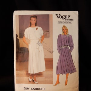 May include: Vogue Patterns Paris Original sewing pattern for a dress by Guy Laroche. The pattern shows two models wearing different versions of the dress. One model is wearing a white dress with a belt, and the other model is wearing a purple dress with a belt. The pattern number is 1553.