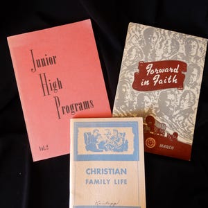 May include: Three vintage books with red, brown, and cream covers. The book on the left is titled "Junior High Programs" with the volume number "Vol. 2". The book in the middle is titled "Christian Family Life" with the author's name "Kentopp" and the text "By Earl S. Rudisill". The book on the right is titled "Forward in Faith" with the word "MARCH" printed on the bottom right corner.
