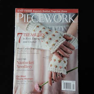 May include: A magazine cover for Piecework magazine featuring a close-up of a pair of white knitted fingerless gloves with pink rosebud embroidery. The magazine cover text reads "7 Treasures to Knit, Embroider, and Crochet".