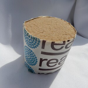 May include: A cylindrical roll of tan-colored fabric with a soft, textured surface. The fabric is wrapped in a paper sleeve with a blue polka dot pattern and the word "re" printed in brown.