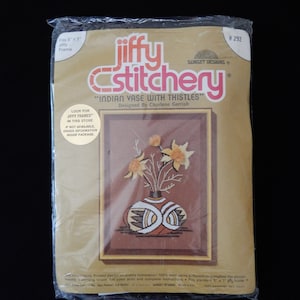 May include: A Jiffy Stitchery embroidery kit featuring a brown vase with yellow flowers and the text "Indian Vase with Thistles". The kit is designed by Charlene Gerrish and fits a 5x7 inch Jiffy frame.