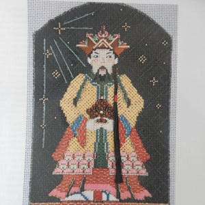 May include: A needlepoint canvas labeled Kit #6 featuring a stylized figure in a yellow robe with red and blue accents, a tall headdress, and a long black braid. The figure stands against a dark background with white star-like patterns and rays.