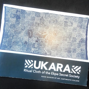 May include: A rectangular print featuring a blue and white checkered pattern with intricate symbols and animal figures. Below the image, the text reads UKARA Ritual Cloth of the Ekpe Secret Society, Hood Museum of Art, Dartmouth College.
