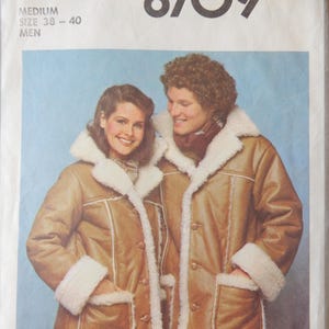 May include: Simplicity 8709 sewing pattern featuring two people wearing tan faux-leather coats with white faux-fur trim. The coats have large pockets and button closures. The pattern is for a medium size, 38-40, for men.