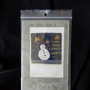 May include: A pattern for a 11" x 11" hooked rug depicting a snowman in a snowy forest scene. The pattern is part of a series of six that can be attached together to form a 22" x 33" Christmas rug. The pattern is titled "9141 Yule Rug I" and is from the "Heart to Hand" collection.