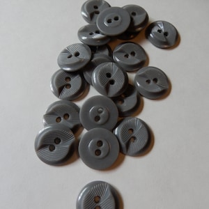 May include: A pile of gray plastic buttons with two holes each. The buttons have a decorative design on the front.
