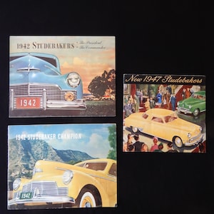 May include: Three vintage Studebaker car brochures. The top brochure features a blue 1942 Studebaker President and Commander. The middle brochure features a yellow 1942 Studebaker Champion. The bottom brochure features a yellow 1947 Studebaker.