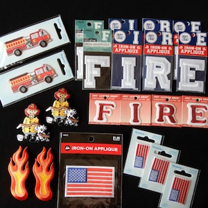 May include: A collection of iron-on appliques featuring fire trucks, firefighters, flames, and the word "FIRE" in various styles. There are also three small American flag appliques.